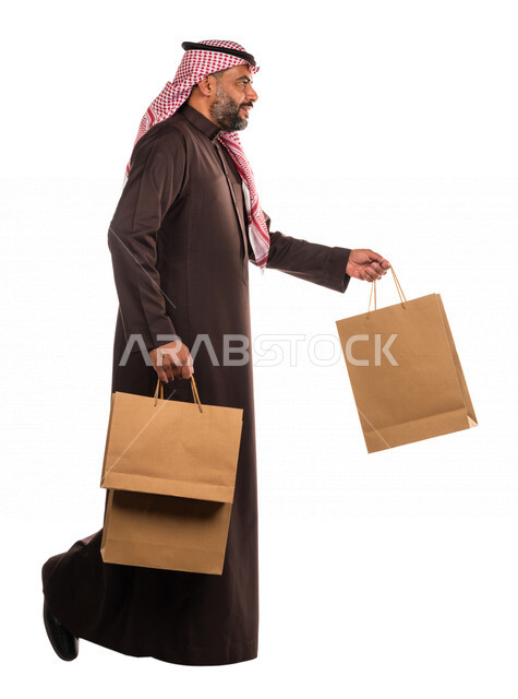 بورتريه لرجل عربي خليجي سعودي يحمل مشترياته، العوده من السوق، متعة التسوق، شراء الأغراض الضروريه، التصفيات والخصومات، الجمعة السوداء، الجمعة البيضاء، الحسومات والتنزيلات، رجل سعودي يحمل اكياس التسوق، صورة الجسم بالطول الكامل، خلفية بيضاء
