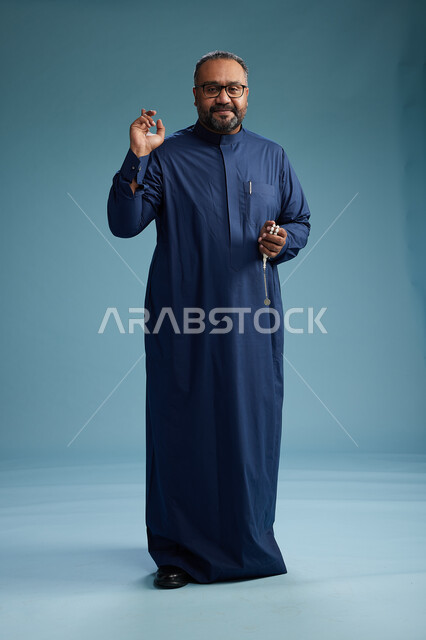 بورتريه لرجل سعودي يقف مرتدياً ثوب كحلي يقوم بايماءات وحركات متنوعه, الوقوف بكامل الجسم, خلفيه زرقاء