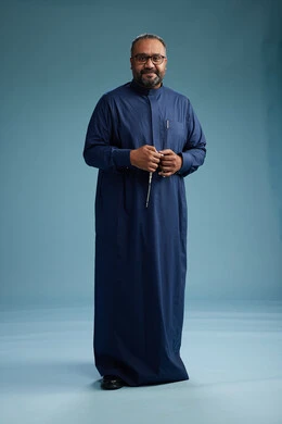 بورتريه لرجل سعودي يقف مرتدياً ثوب كحلي يقوم بايماءات وحركات متنوعه, الوقوف بكامل الجسم, خلفيه زرقاء