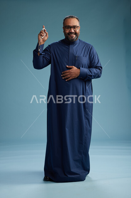 بورتريه لرجل سعودي يقف مرتدياً ثوب كحلي يقوم بايماءات وحركات متنوعه, الوقوف بكامل الجسم, خلفيه زرقاء