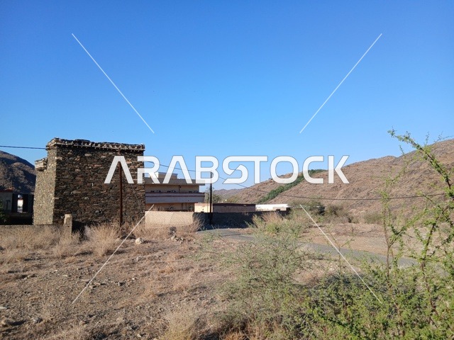 The old stone houses on the mountains in the Al-Baha region in the archaeological village of Dhai Ain in southern Saudi Arabia, famous historical tourist landmarks, and the green trees and plants surrounding the village on the highlands and mountain peaks.