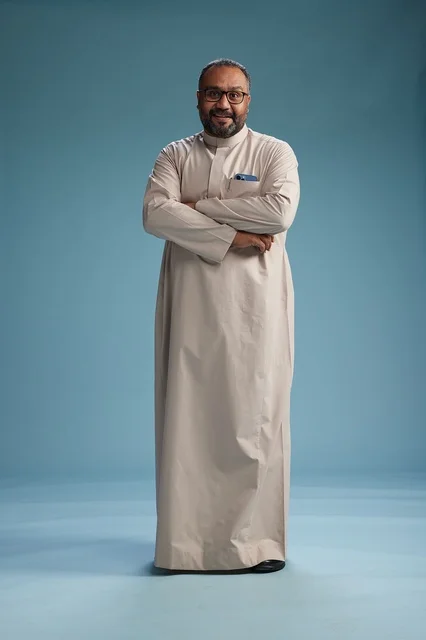 A smiling Saudi man wearing a beige thobe with various hand gestures and movements, full body, blue background.