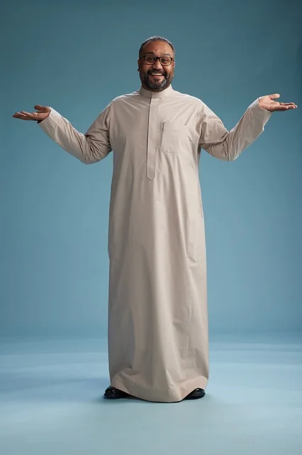A smiling Saudi man wearing a beige thobe with various hand gestures and movements, full body, blue background.