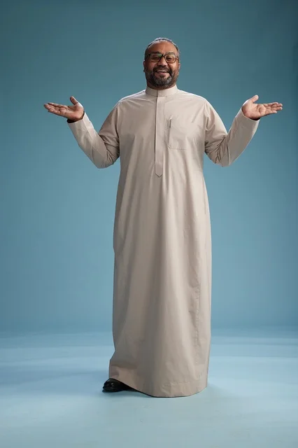 A smiling Saudi man wearing a beige thobe with various hand gestures and movements, full body, blue background.
