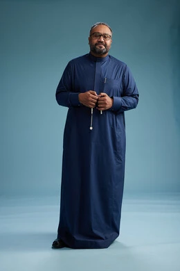 A portrait of a Saudi man standing wearing a navy blue thobe, making various gestures and movements, standing full body, with a blue background.