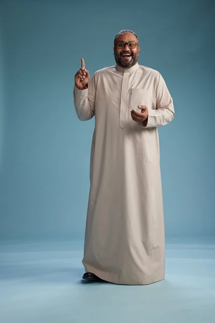 A smiling Saudi man wearing a beige thobe with various hand gestures and movements, full body, blue background.