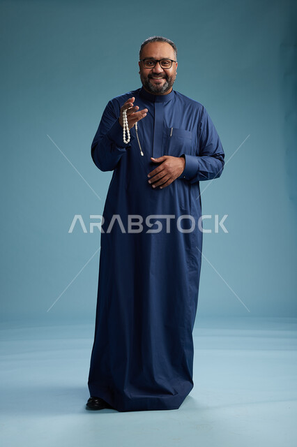 بورتريه لرجل سعودي يقف مرتدياً ثوب كحلي يقوم بايماءات وحركات متنوعه, الوقوف بكامل الجسم, خلفيه زرقاء