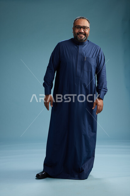 A portrait of a Saudi man standing wearing a navy blue thobe, making various gestures and movements, standing full body, with a blue background.