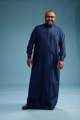 بورتريه لرجل سعودي يقف مرتدياً ثوب كحلي يقوم بايماءات وحركات متنوعه, الوقوف بكامل الجسم, خلفيه زرقاء