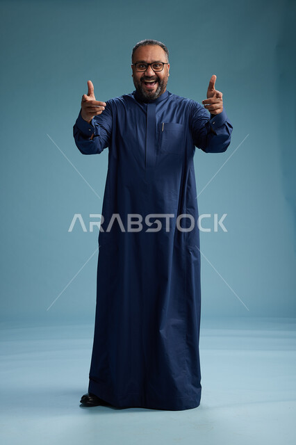 بورتريه لرجل سعودي يقف مرتدياً ثوب كحلي يقوم بايماءات وحركات متنوعه, الوقوف بكامل الجسم, خلفيه زرقاء