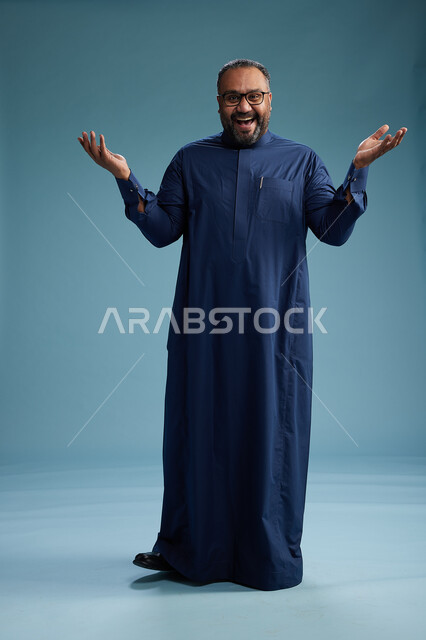 بورتريه لرجل سعودي يقف مرتدياً ثوب كحلي يقوم بايماءات وحركات متنوعه, الوقوف بكامل الجسم, خلفيه زرقاء