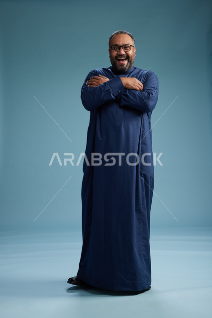بورتريه لرجل سعودي يقف مرتدياً ثوب كحلي يقوم بايماءات وحركات متنوعه, الوقوف بكامل الجسم, خلفيه زرقاء
