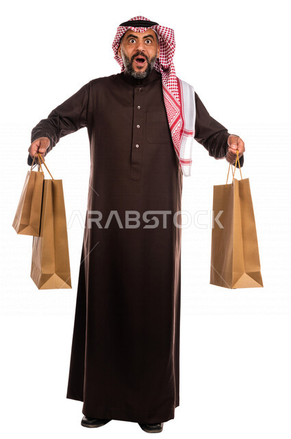 بورتريه لرجل عربي خليجي سعودي يحمل مشترياته، العوده من السوق، متعة التسوق، شراء الأغراض الضروريه، التصفيات والخصومات، الجمعة السوداء، الجمعة البيضاء، الحسومات والتنزيلات، رجل سعودي يحمل اكياس التسوق، صورة الجسم بالطول الكامل، خلفية بيضاء
