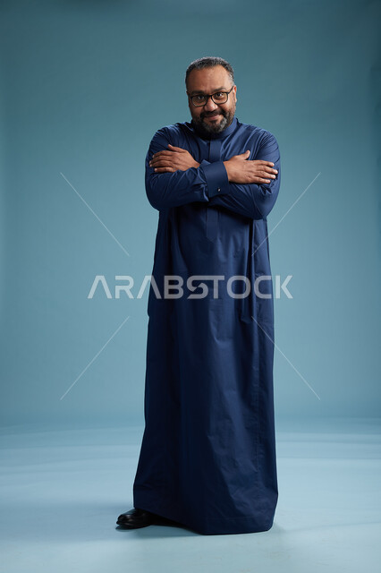 بورتريه لرجل سعودي يقف مرتدياً ثوب كحلي يقوم بايماءات وحركات متنوعه, الوقوف بكامل الجسم, خلفيه زرقاء