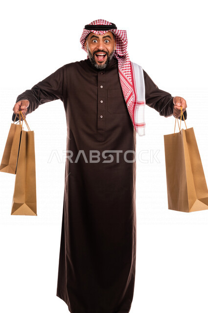 بورتريه لرجل عربي خليجي سعودي يحمل مشترياته، العوده من السوق، متعة التسوق، شراء الأغراض الضروريه، التصفيات والخصومات، الجمعة السوداء، الجمعة البيضاء، الحسومات والتنزيلات، رجل سعودي يحمل اكياس التسوق، صورة الجسم بالطول الكامل، خلفية بيضاء