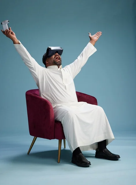 بورتريه لرجل سعودي يرتدي نظارة واقع افتراضي ويمسك بوحدة تحكم, الاستمتاع بالعاب الفيديو, خلفيه زرقاء