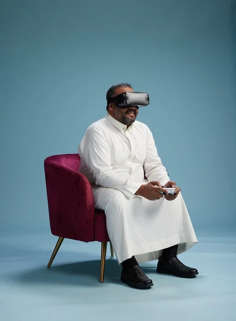 بورتريه لرجل سعودي يرتدي نظارة واقع افتراضي ويمسك بوحدة تحكم, الاستمتاع بالعاب الفيديو, خلفيه زرقاء