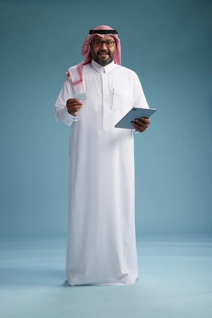 A Saudi man in traditional attire using a tablet and a credit card, the concept of electronic payment, online shopping, blue background, full body.