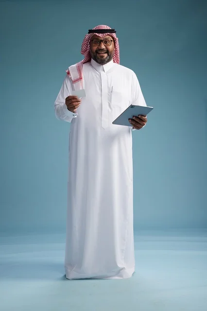 A Saudi man in traditional attire using a tablet and a credit card, the concept of electronic payment, online shopping, blue background, full body.