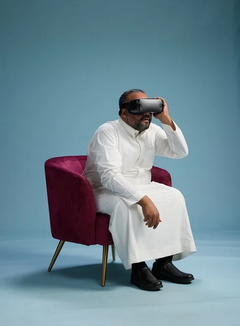 A Saudi man in traditional attire is experiencing virtual reality, watching VR movies, with a blue background.