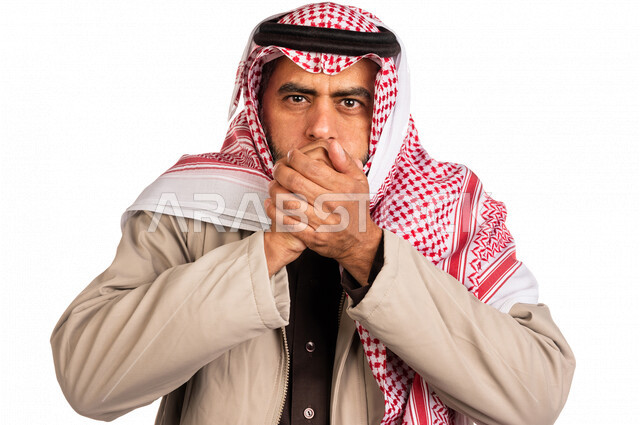 بورتريه لرجل عربي خليجي سعودي يرتدي ملابس الشتاء الدافئة وينفخ بيده، الشعور بالصقيع، ارتداء جاكيت الشتاء، التنفس على اليدين لابقائها دافئة، ايماءات وجه ويدين تدل على البرد الشديد، اجواء شتوية، خلفية بيضاء