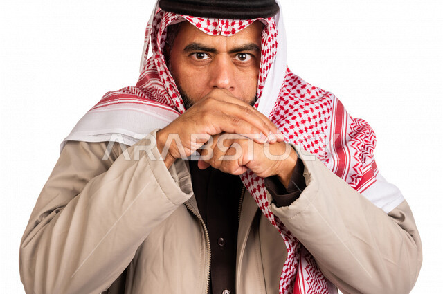 بورتريه لرجل عربي خليجي سعودي يرتدي ملابس الشتاء الدافئة وينفخ بيده، الشعور بالصقيع، ارتداء جاكيت الشتاء، التنفس على اليدين لابقائها دافئة، ايماءات وجه ويدين تدل على البرد الشديد، اجواء شتوية، خلفية بيضاء