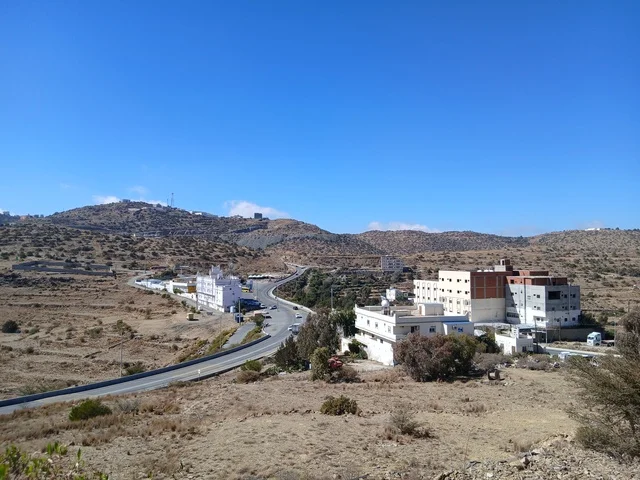 البيوت السكنية والطرقات المهيئة في المدينة، المعالم السياحية التاريخية المشهورة، منطقة الباحة في قرية ذي العين الأثرية جنوب المملكة العربية السعودية، الأشجار والنباتات الخضراء المحيطة بالقرية على المرتفعات والقمم الجبلية