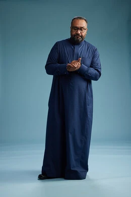 A portrait of a Saudi man standing wearing a navy blue thobe, making various gestures and movements, standing full body, with a blue background.