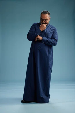 A portrait of a Saudi man standing wearing a navy blue thobe, making various gestures and movements, standing full body, with a blue background.