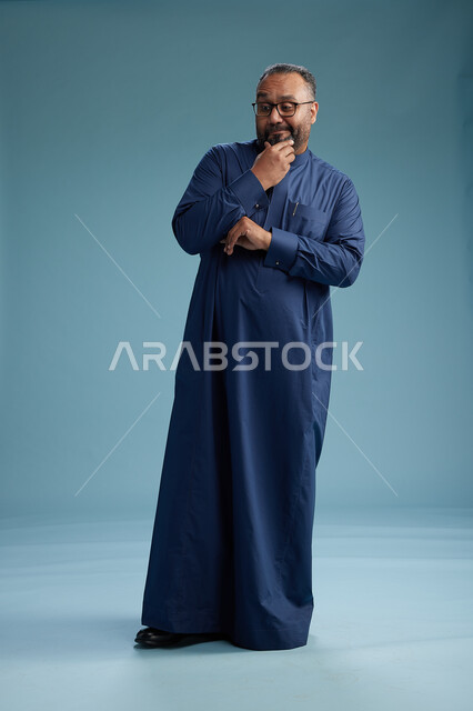 بورتريه لرجل سعودي يقف مرتدياً ثوب كحلي يقوم بايماءات وحركات متنوعه, الوقوف بكامل الجسم, خلفيه زرقاء