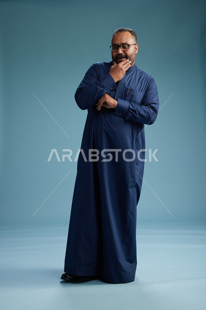 بورتريه لرجل سعودي يقف مرتدياً ثوب كحلي يقوم بايماءات وحركات متنوعه, الوقوف بكامل الجسم, خلفيه زرقاء