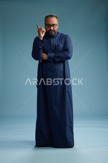 بورتريه لرجل سعودي يقف مرتدياً ثوب كحلي يقوم بايماءات وحركات متنوعه, الوقوف بكامل الجسم, خلفيه زرقاء