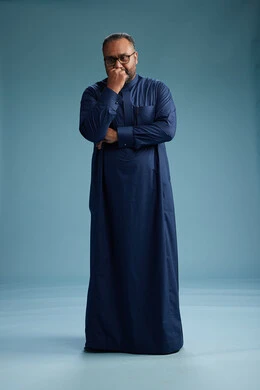 A portrait of a Saudi man standing wearing a navy blue thobe, making various gestures and movements, standing full body, with a blue background.