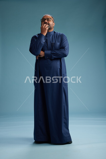 بورتريه لرجل سعودي يقف مرتدياً ثوب كحلي يقوم بايماءات وحركات متنوعه, الوقوف بكامل الجسم, خلفيه زرقاء