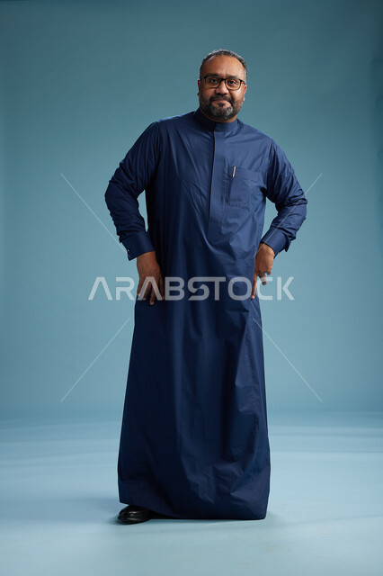 بورتريه لرجل سعودي يقف مرتدياً ثوب كحلي يقوم بايماءات وحركات متنوعه, الوقوف بكامل الجسم, خلفيه زرقاء
