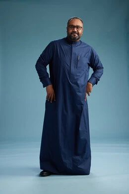 بورتريه لرجل سعودي يقف مرتدياً ثوب كحلي يقوم بايماءات وحركات متنوعه, الوقوف بكامل الجسم, خلفيه زرقاء