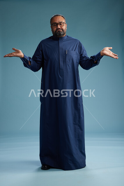 A portrait of a Saudi man standing wearing a navy blue thobe, making various gestures and movements, standing full body, with a blue background.
