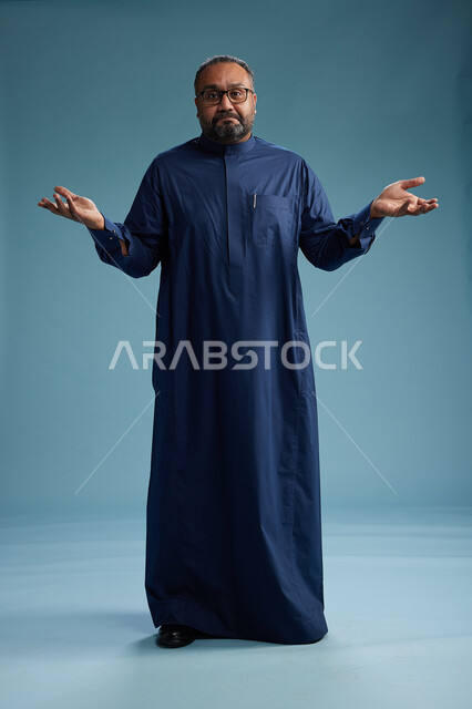 بورتريه لرجل سعودي يقف مرتدياً ثوب كحلي يقوم بايماءات وحركات متنوعه, الوقوف بكامل الجسم, خلفيه زرقاء
