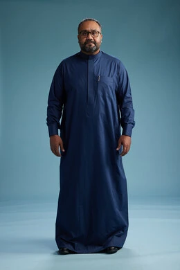 A portrait of a Saudi man standing wearing a navy blue thobe, making various gestures and movements, standing full body, with a blue background.