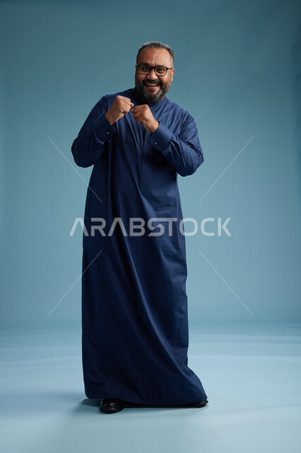 A portrait of a Saudi man standing wearing a navy blue thobe, making various gestures and movements, standing full body, with a blue background.