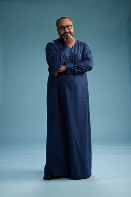 A portrait of a Saudi man standing wearing a navy blue thobe, making various gestures and movements, standing full body, with a blue background.