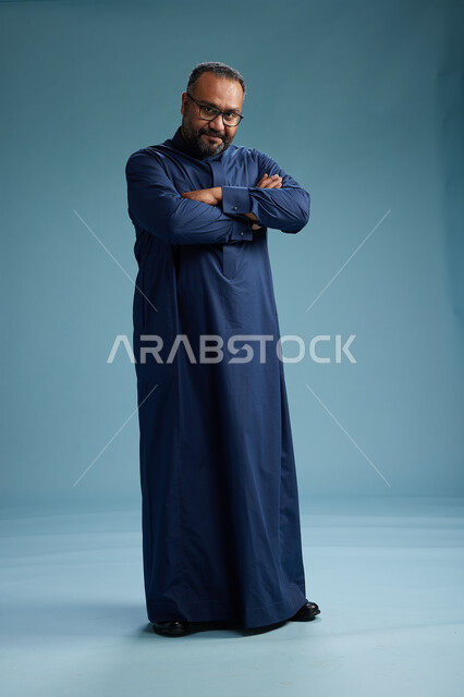 بورتريه لرجل سعودي يقف مرتدياً ثوب كحلي يقوم بايماءات وحركات متنوعه, الوقوف بكامل الجسم, خلفيه زرقاء