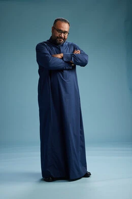 A portrait of a Saudi man standing wearing a navy blue thobe, making various gestures and movements, standing full body, with a blue background.