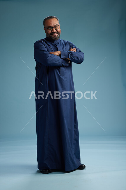 بورتريه لرجل سعودي يقف مرتدياً ثوب كحلي يقوم بايماءات وحركات متنوعه, الوقوف بكامل الجسم, خلفيه زرقاء