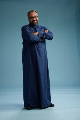 A portrait of a Saudi man standing wearing a navy blue thobe, making various gestures and movements, standing full body, with a blue background.