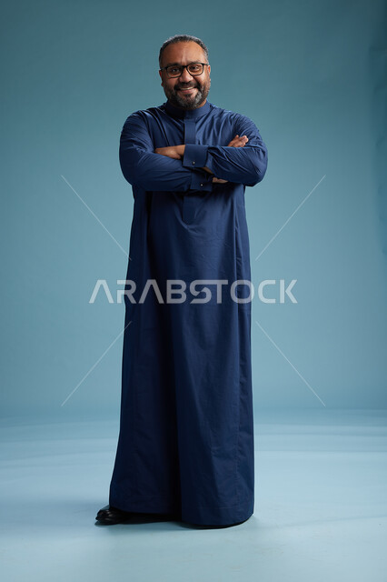 بورتريه لرجل سعودي يقف مرتدياً ثوب كحلي يقوم بايماءات وحركات متنوعه, الوقوف بكامل الجسم, خلفيه زرقاء