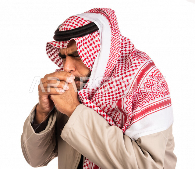 بورتريه لرجل عربي خليجي سعودي يرتدي ملابس الشتاء الدافئة وينفخ بيده، الشعور بالصقيع، ارتداء جاكيت الشتاء، التنفس على اليدين لابقائها دافئة، ايماءات وجه ويدين تدل على البرد الشديد، اجواء شتوية، خلفية بيضاء