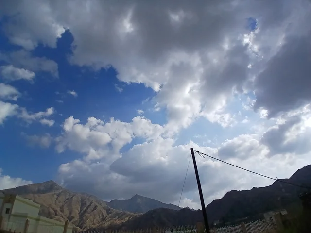 منظر السماء الملبدة بالغيوم في المنطقة الجبلية، المعالم السياحية التاريخية المشهورة، المرتفعات والقمم الجبلية بمنطقة الباحة في قرية ذي العين الأثرية جنوب المملكة العربية السعودية،  البيوت السكنية والطرقات المهيئة في المدينة، الأشجار والنباتات الخضراء