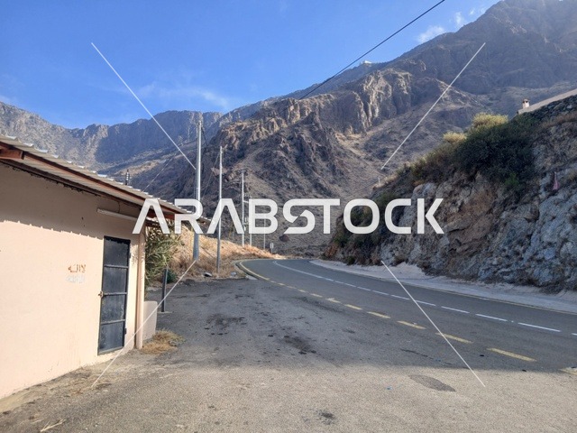 The highlands and mountain peaks in the Al-Baha region in the archaeological village of Dhai Ain, south of the Kingdom of Saudi Arabia, the view of the cloudy sky in the mountainous area, the famous historical tourist landmarks, the residential houses and the paved roads in the city, the trees and green plants.