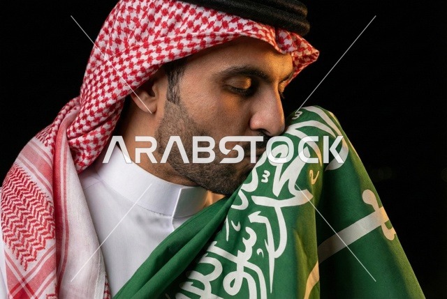 إيماءات الفخر و السرور بالانتماء للوطن, إحياء ذكرى اليوم الوطني السعودي 23 سبتمبر، يوم العلم السعودي 11 مارس, رجل عربي سعودي يرتدي الشماغ والثوب التقليدي يقبل علم المملكة، يوم بدينا 1727 م